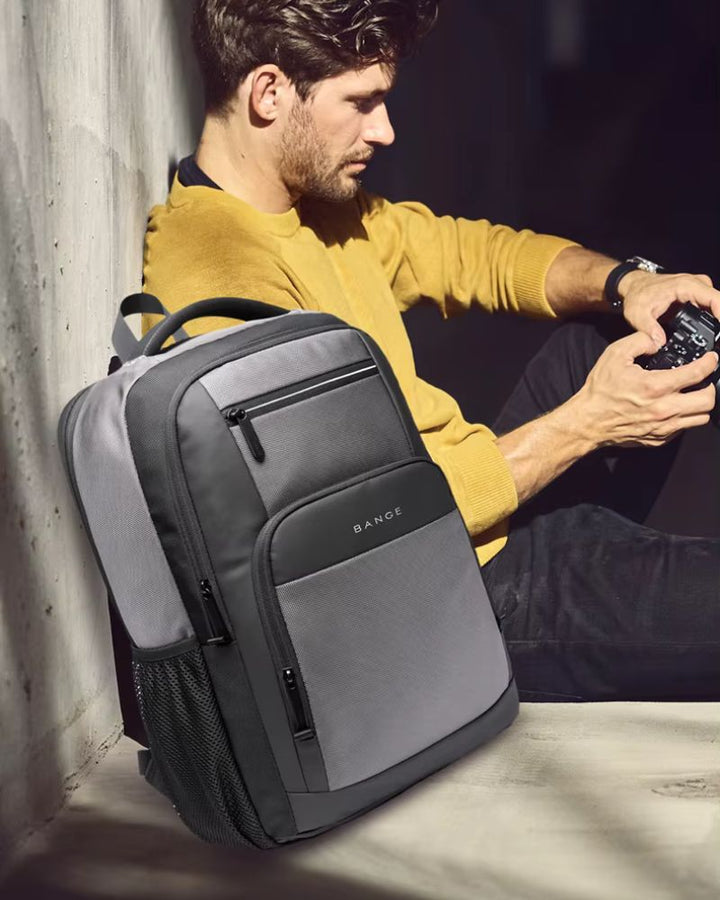 Sac à dos avec pochette ordinateur, coloris gris, posé à côté d'un homme avec un appareil photo