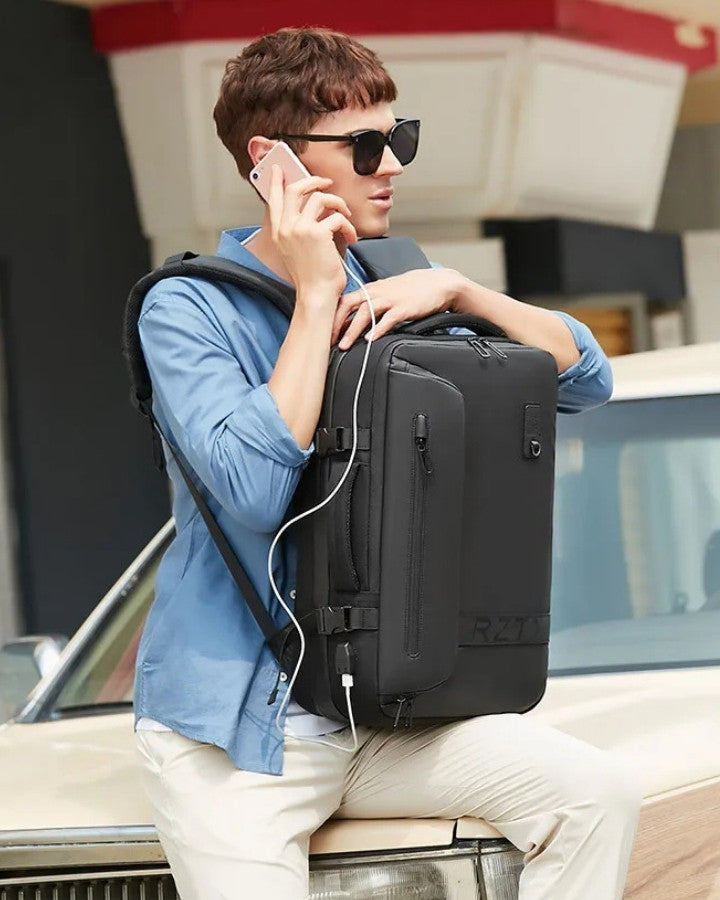 Sac à Dos de Compression Voyage Sans Aspirateur, noir, porté par un homme avec un téléphone à l'oreille, se tenant sur le capot d'une voiture