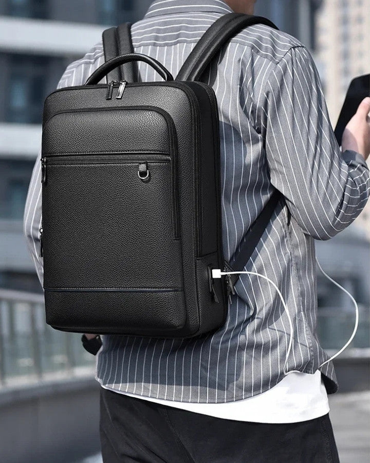 Sac à Dos Homme Similicuir Texturé, porté sur le dos d'un homme tenant son téléphone portable en main, en charge avec le port USB intégré au sac