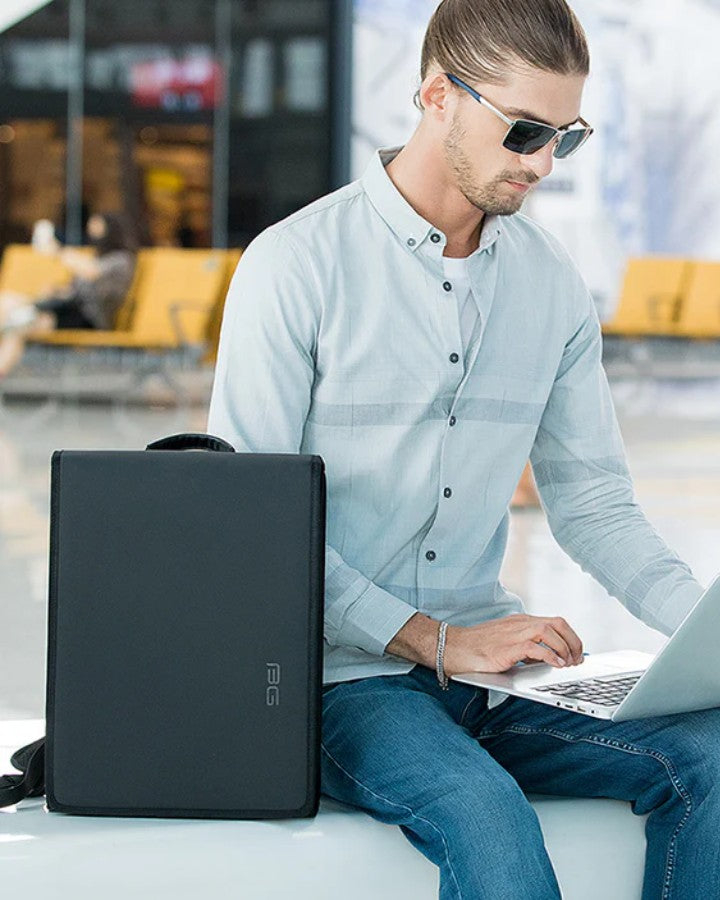 Homme utilisant un ordinateur portable avec le sac à dos plat ordinateur posé à ses côtés dans un espace public.